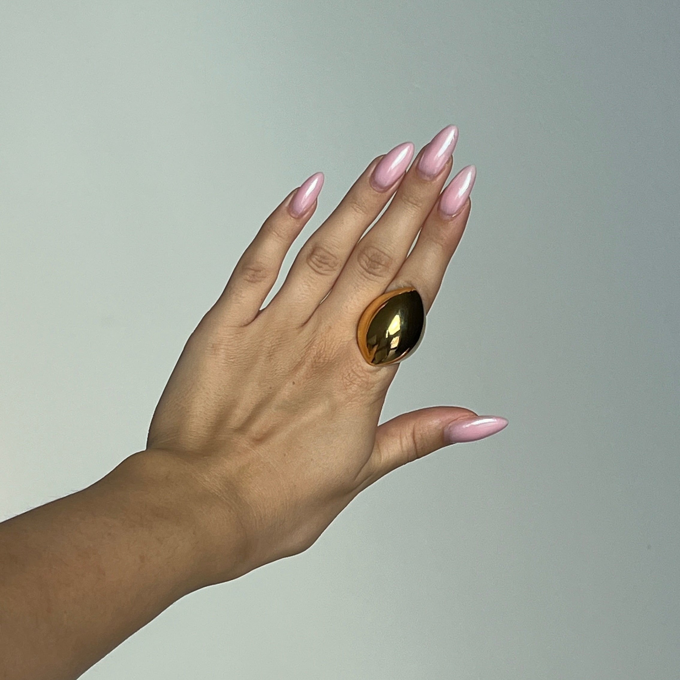 Hand wearing the angular ring in PVD-coated 18k gold-plated stainless steel against a plain grey background