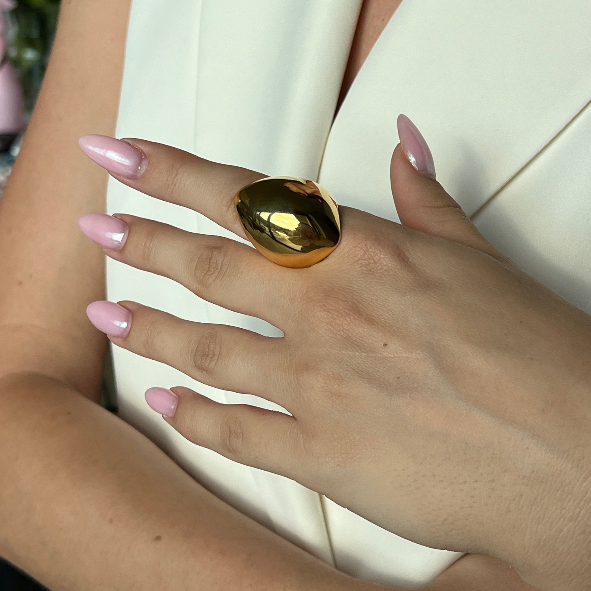 Model in a cream blazer wearing the angular statement ring in PVD-coated 18k gold-plated stainless steel with hand on her arm