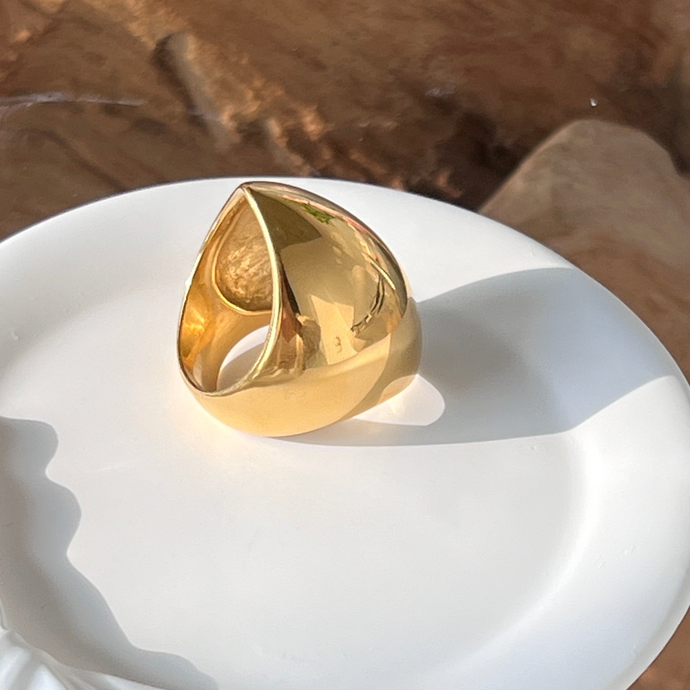 Angular ring in PVD-coated 18k gold-plated stainless steel displayed on a white dish against a wooden background