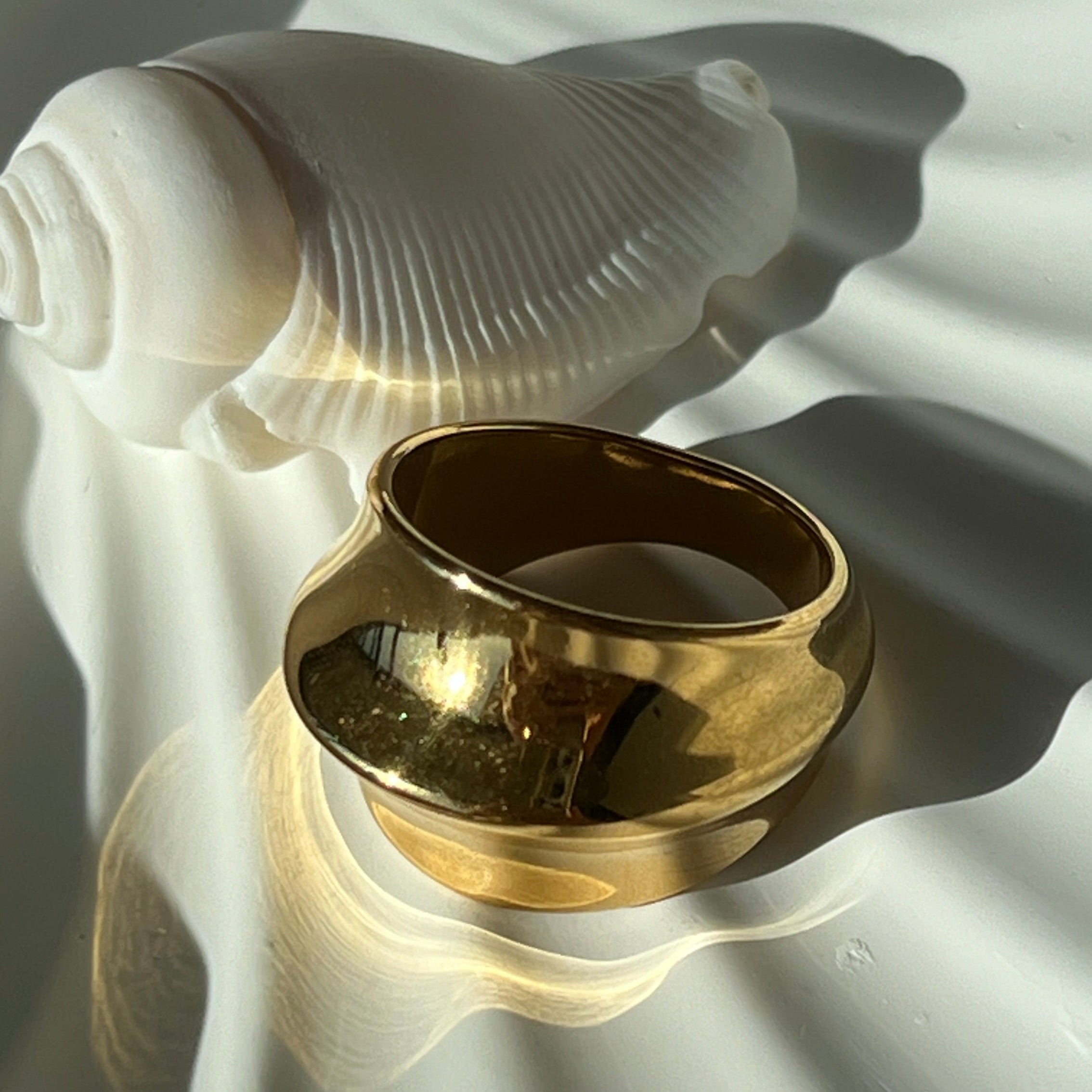 Side view of the fashionable dome ring in PVD-coated 18k gold-plated stainless steel on a white shell-shaped dish in natural light