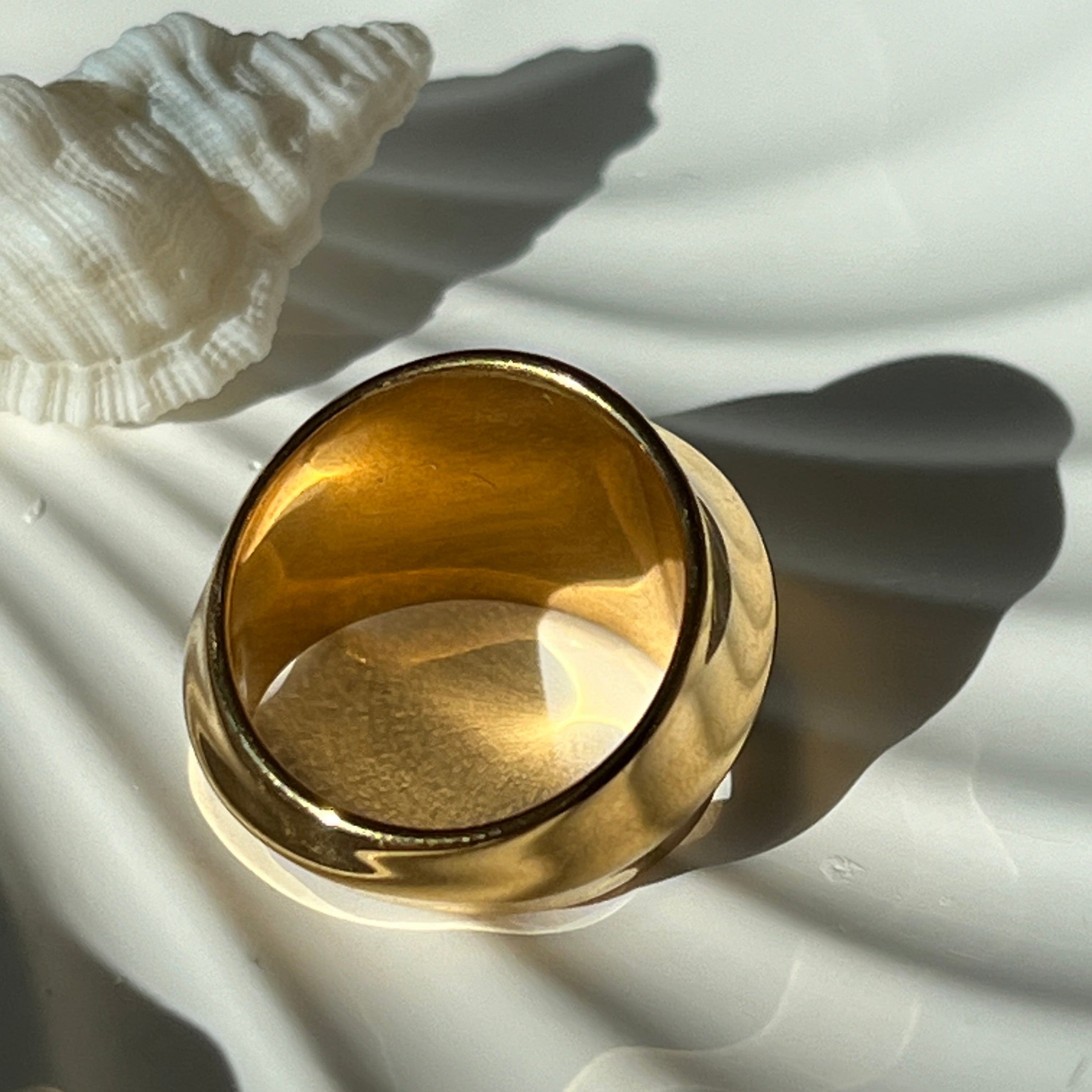 Fashionable dome ring in PVD-coated 18k gold-plated stainless steel lying on a white shell-shaped dish, showing the open band