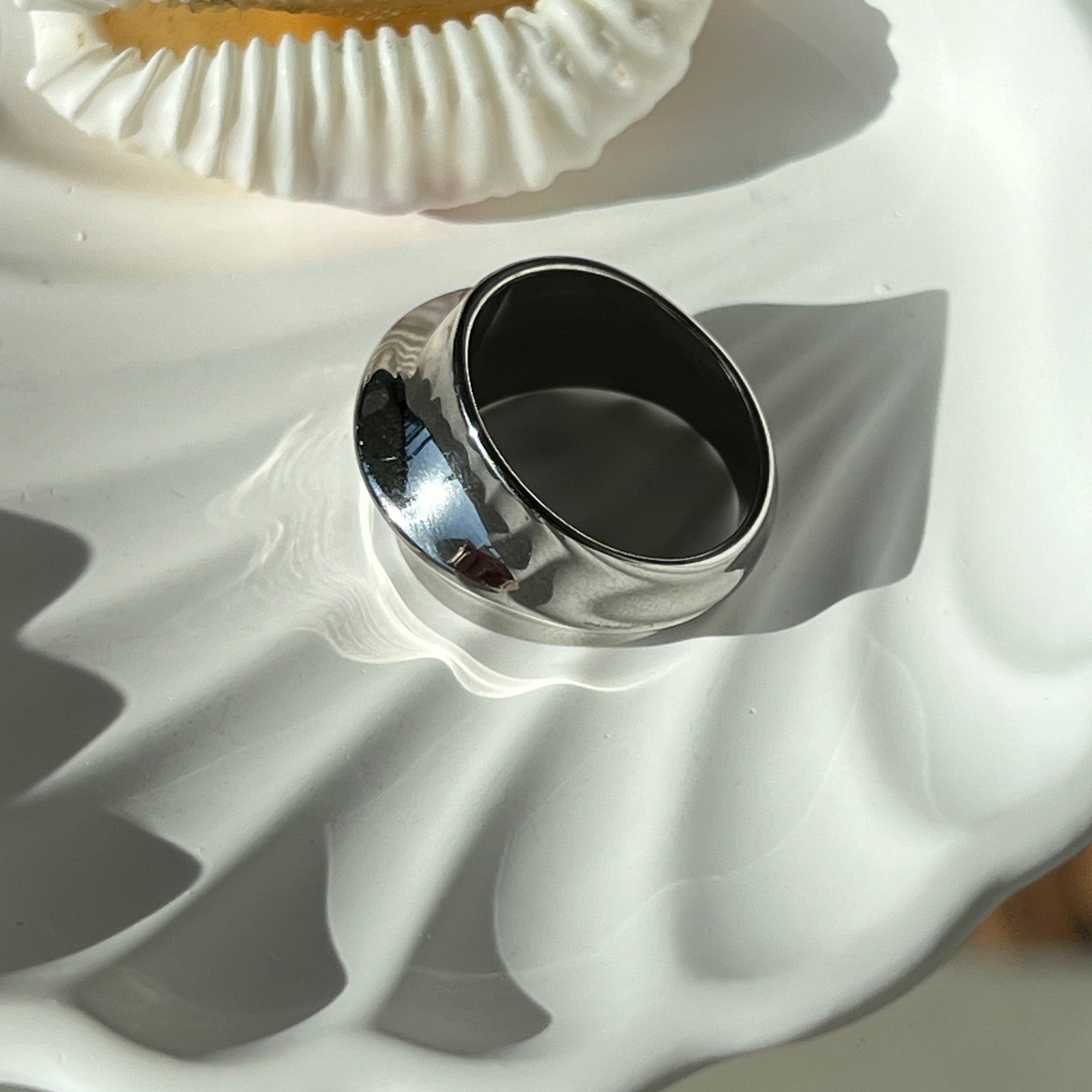 Side view of the fashionable dome ring in PVD-coated 925 silver-plated stainless steel on a white shell-shaped dish