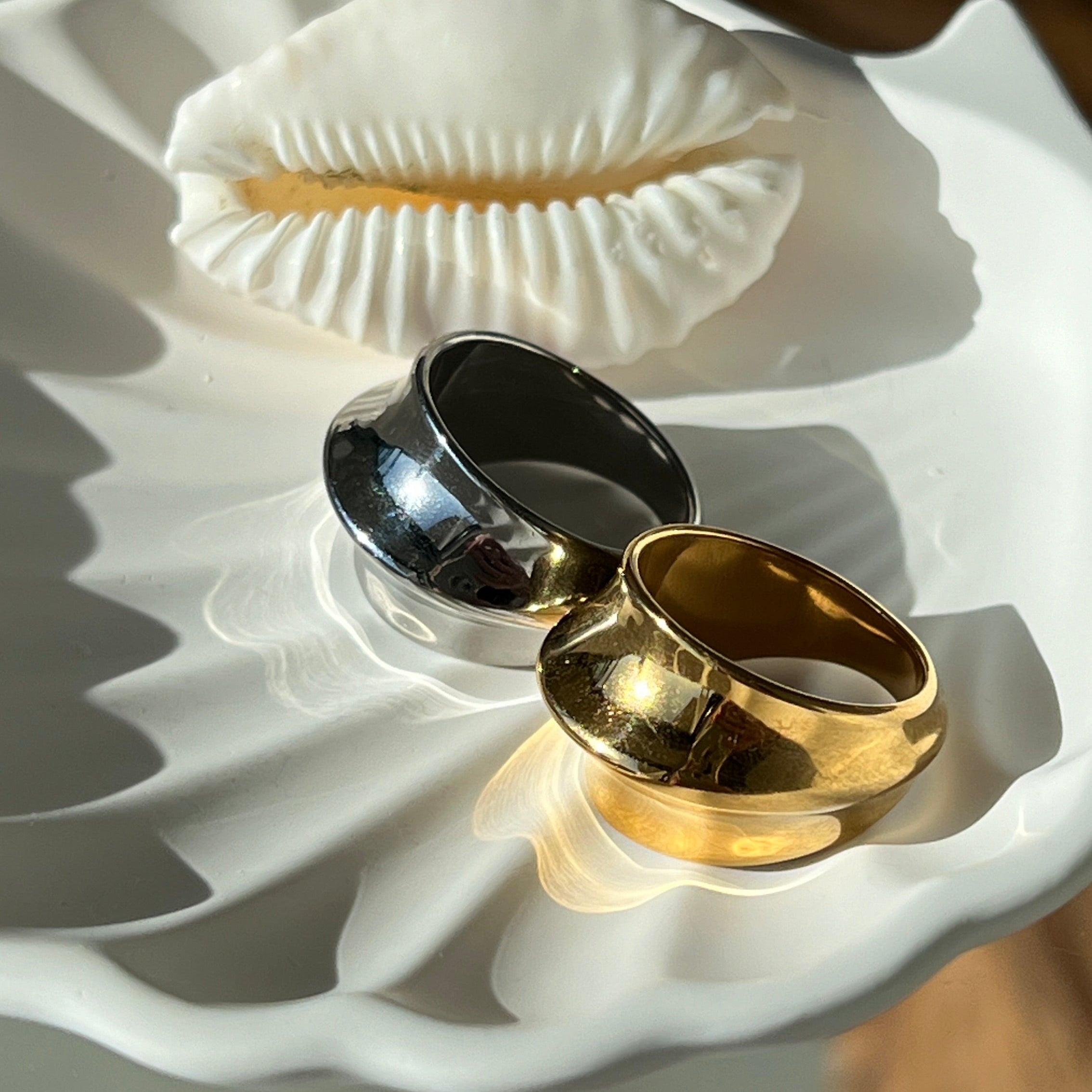 Fashionable dome ring in PVD-coated 925 silver-plated stainless steel shown beside a gold version on a white shell-shaped dish