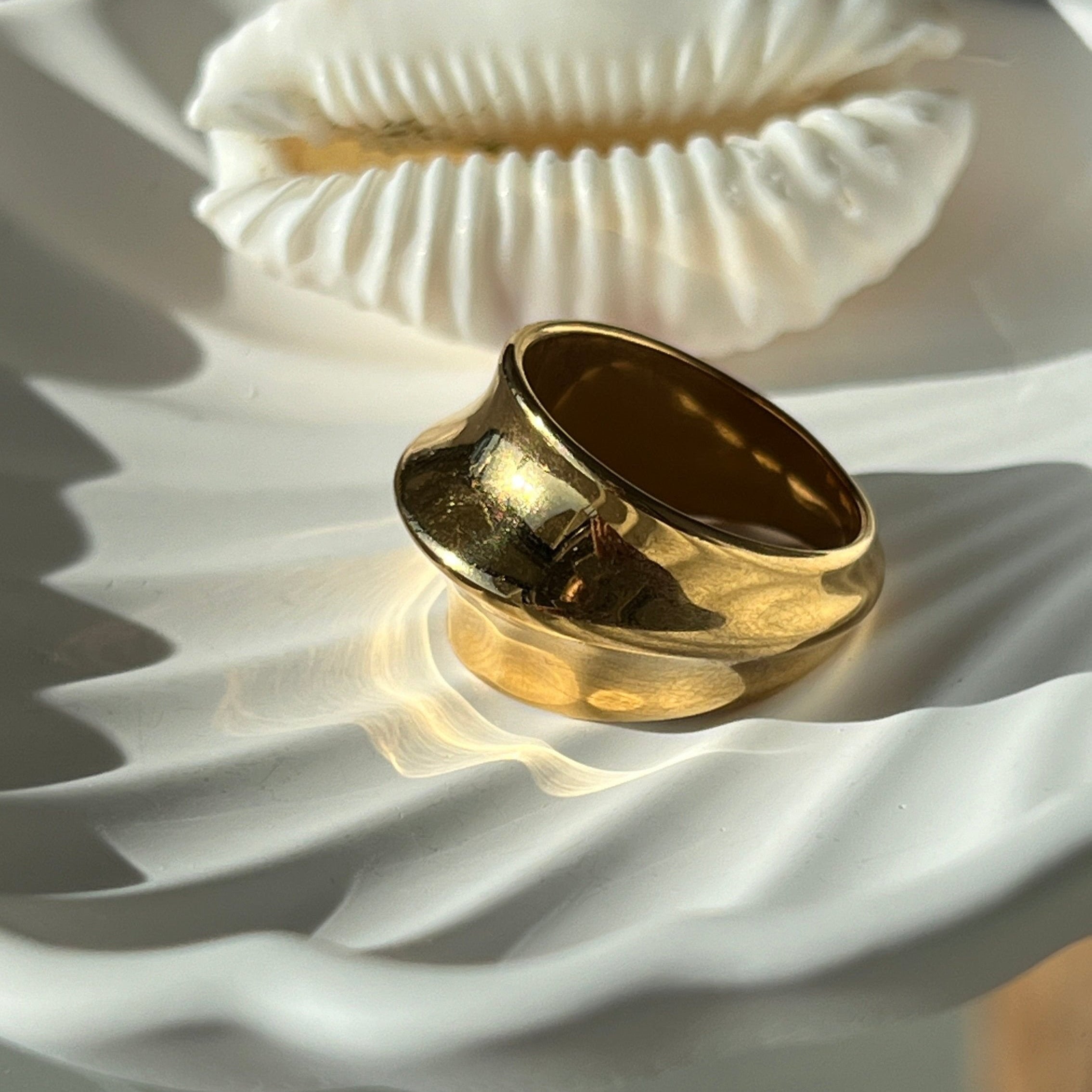 Fashionable dome ring in PVD-coated 18k gold-plated stainless steel displayed on a white shell-shaped dish