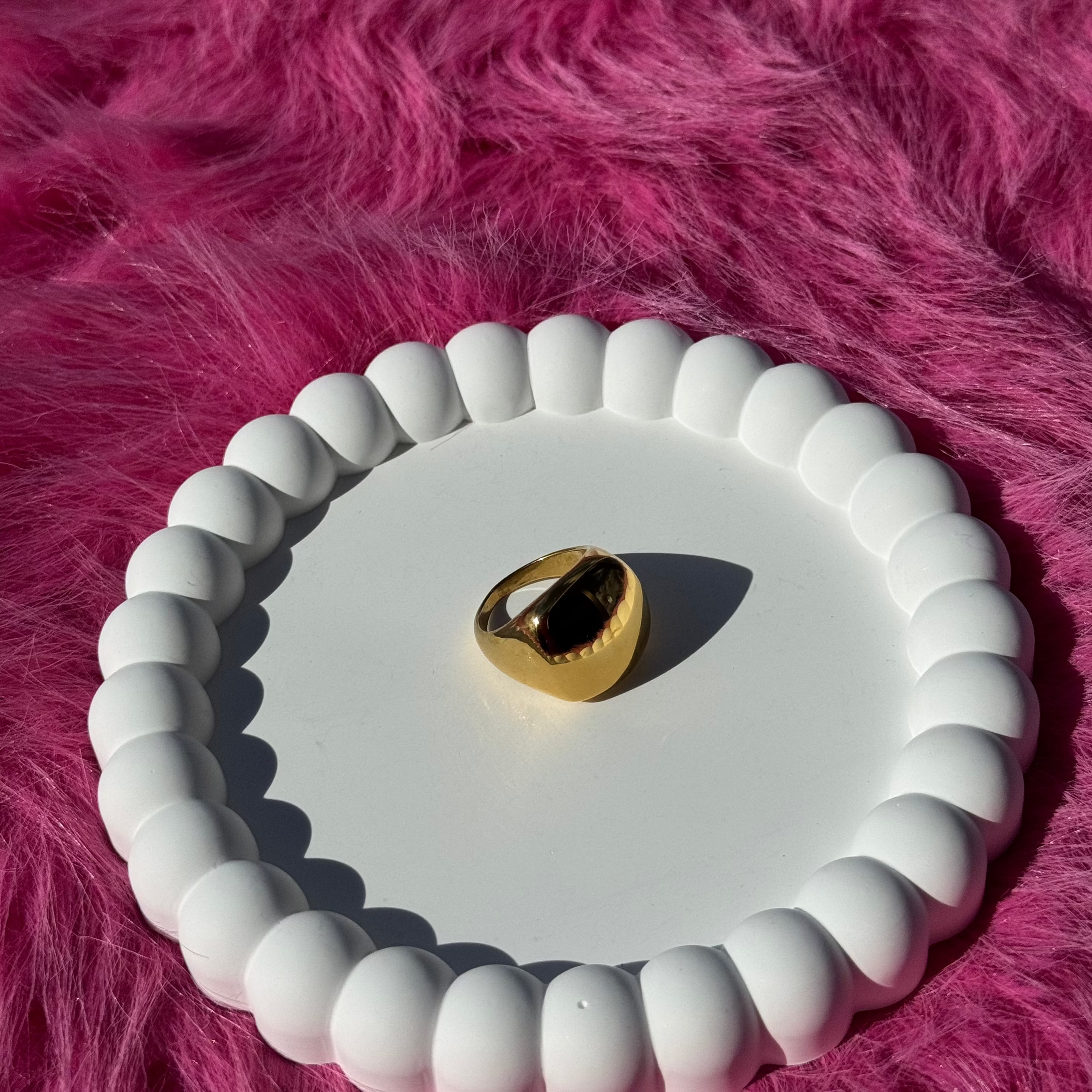 Square signet ring in PVD-coated 18k gold-plated stainless steel displayed on a white beaded dish against a pink fur background