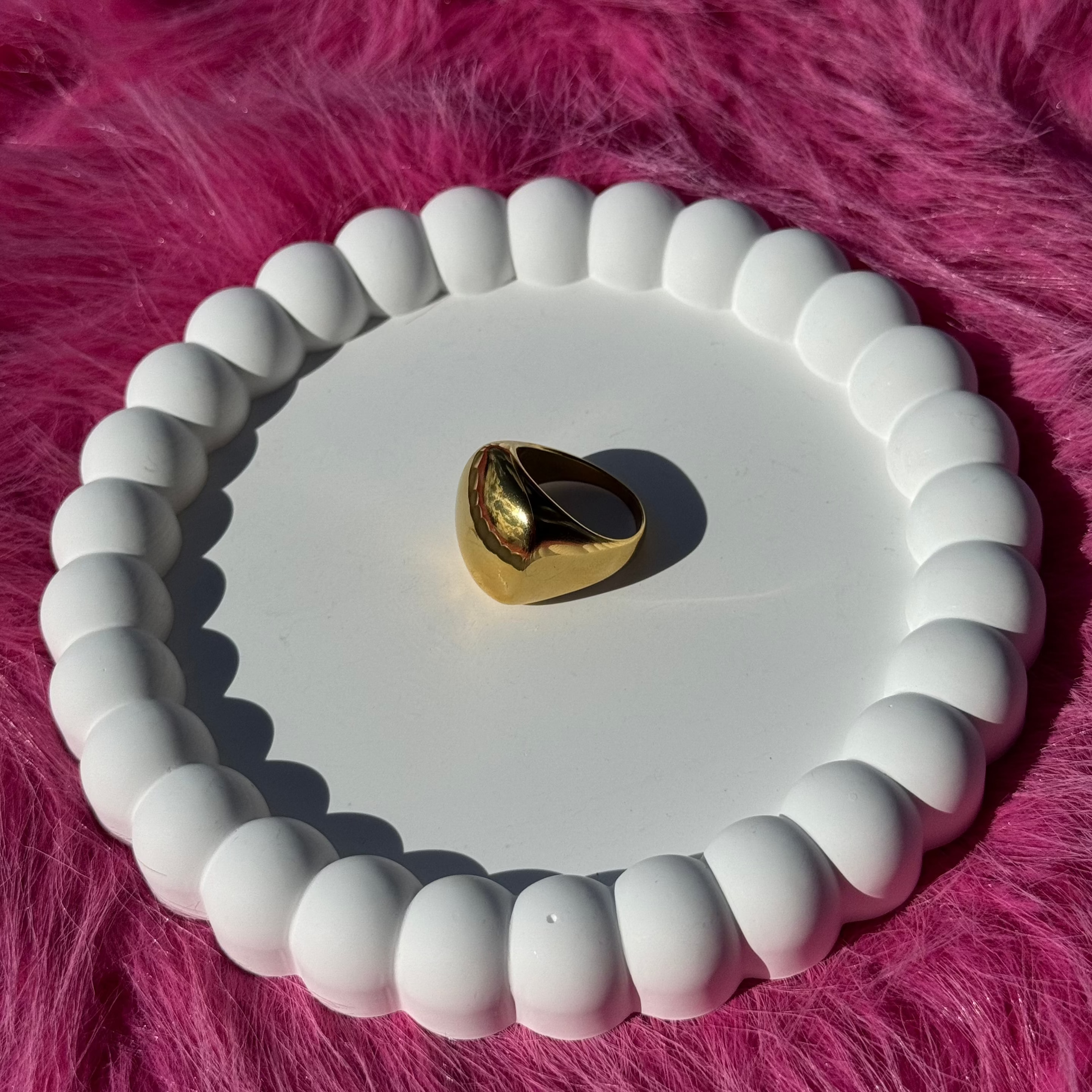 Side view of the square signet ring in PVD-coated 18k gold-plated stainless steel on a white beaded dish against a pink fur background