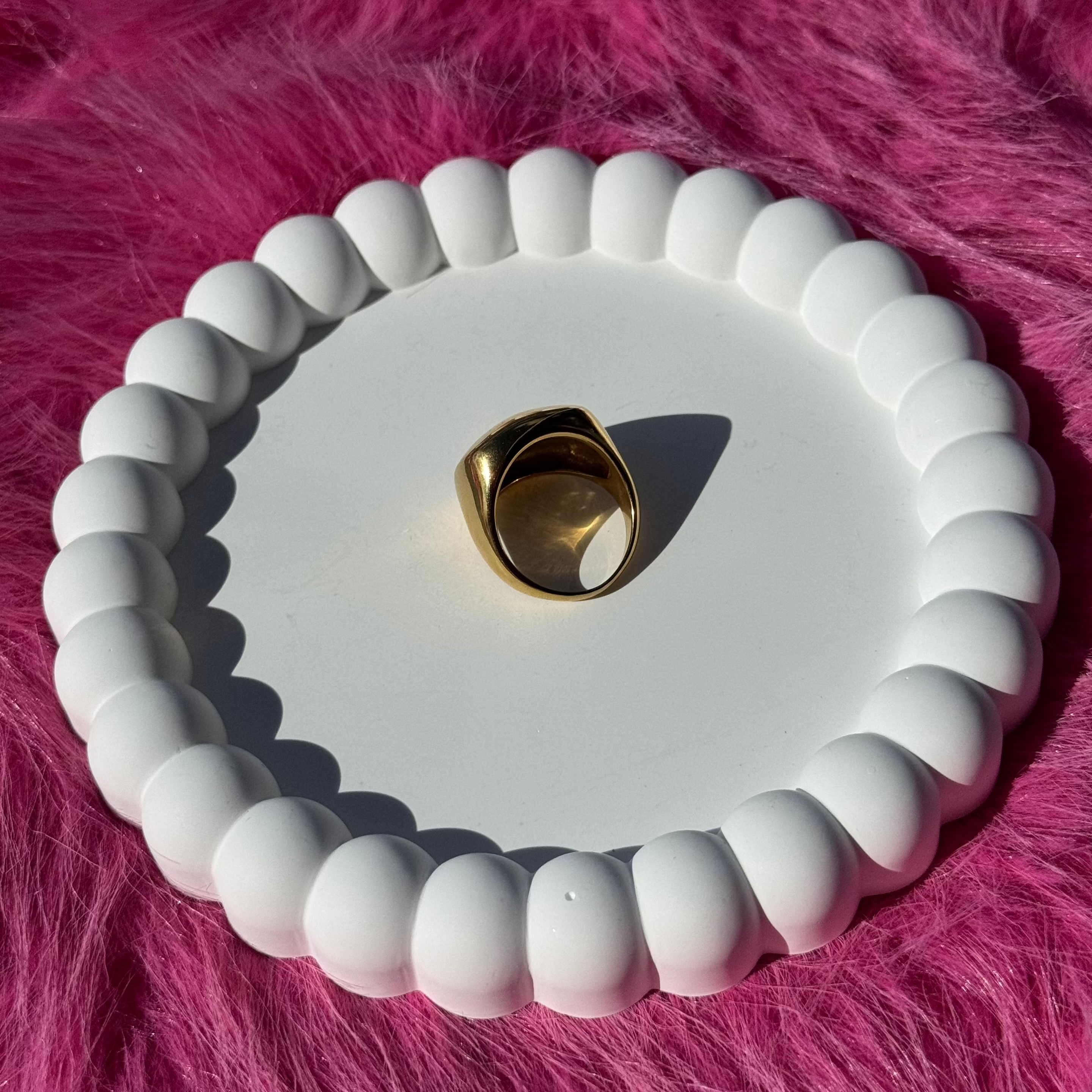 Close-up of the square signet ring in PVD-coated 18k gold-plated stainless steel on a white beaded dish against a pink fur background