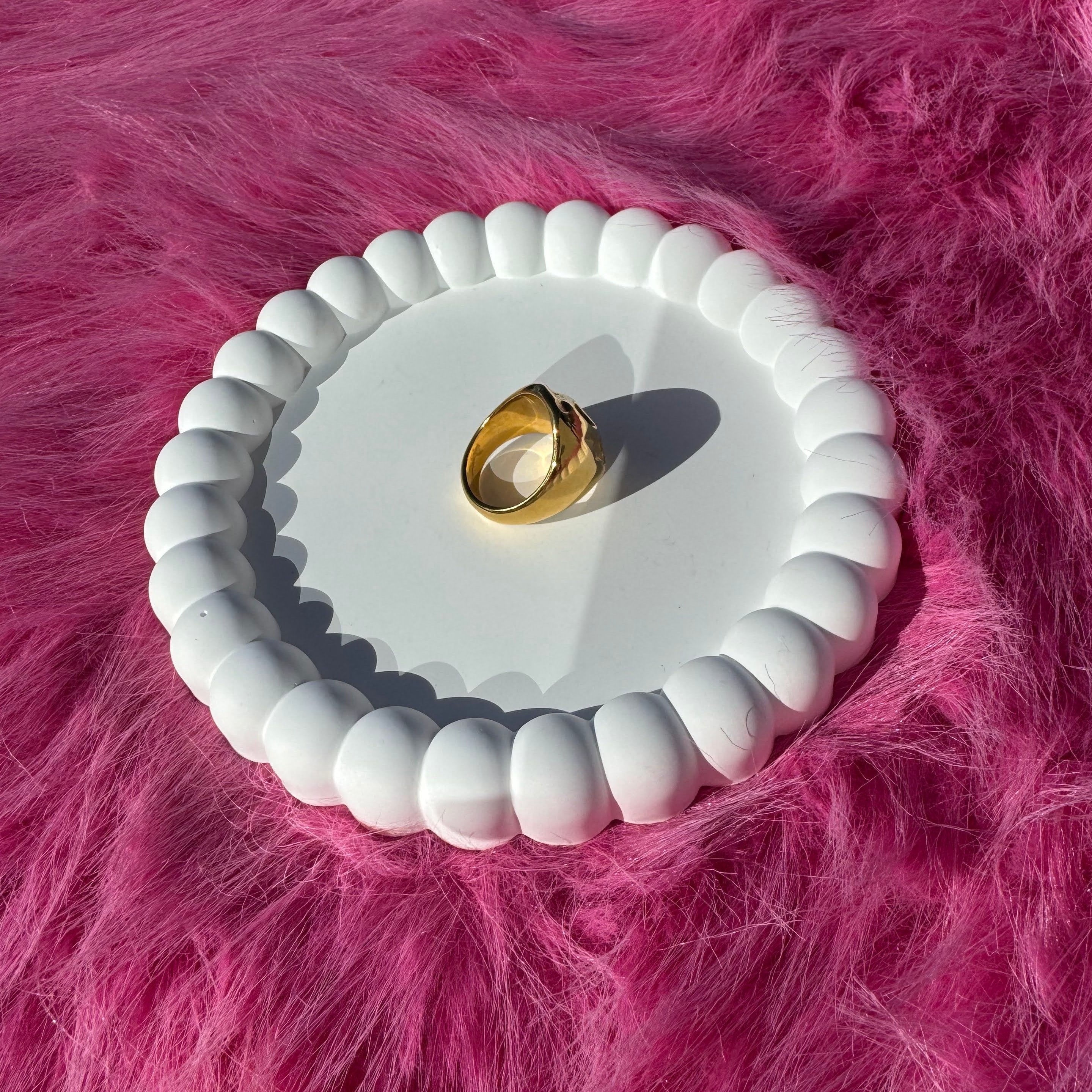 Top view of the irregular bold chunky ring in PVD-coated 18k gold-plated stainless steel on a white beaded dish against a pink fur background
