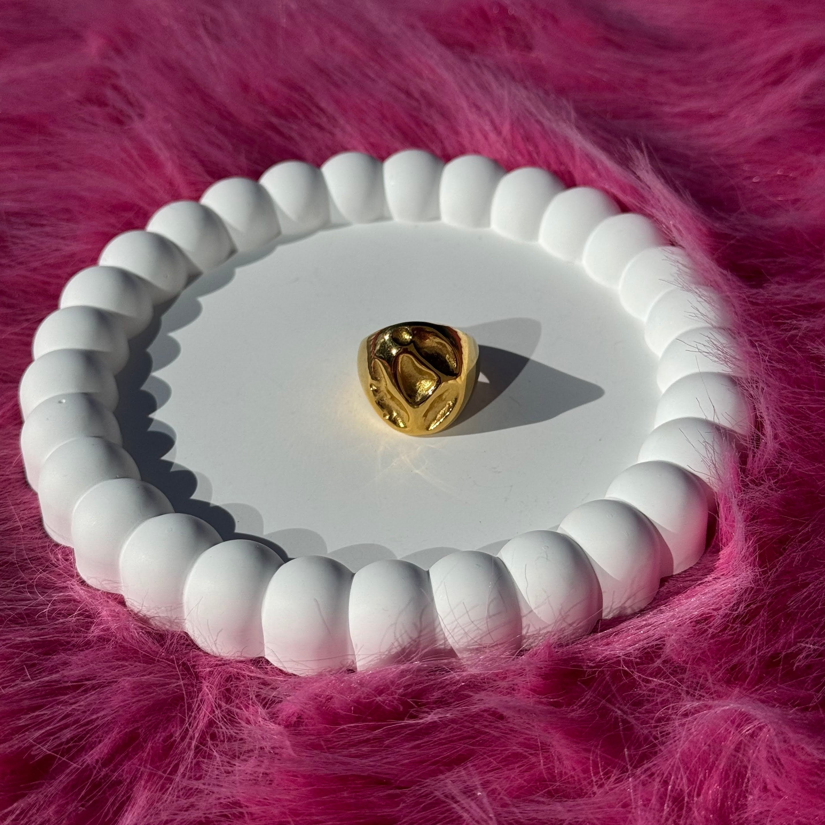 Irregular bold chunky ring in PVD-coated 18k gold-plated stainless steel displayed on a white beaded dish against a pink fur background