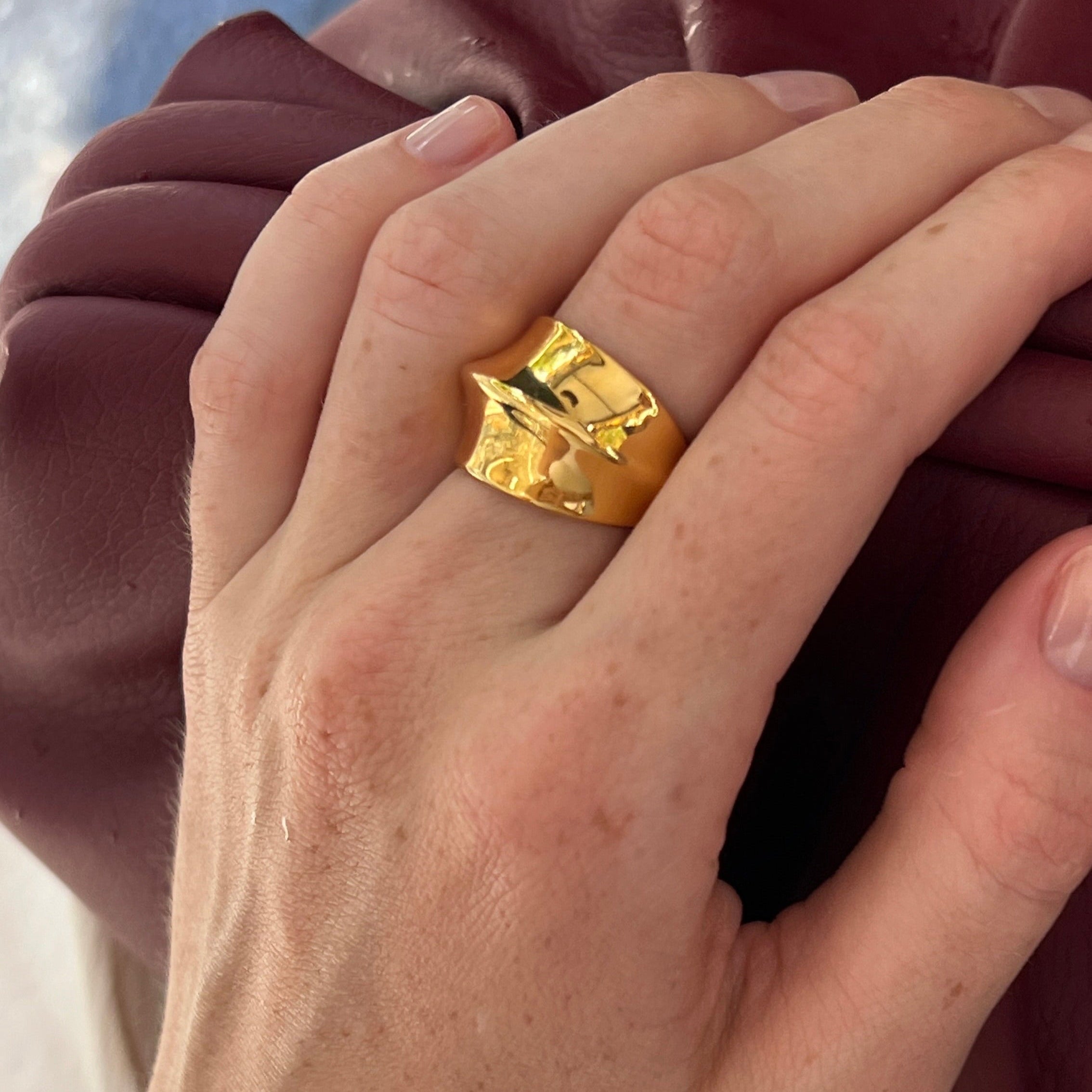 Hands wearing the fashionable dome ring in PVD-coated 18k gold-plated stainless steel against a maroon leather coat