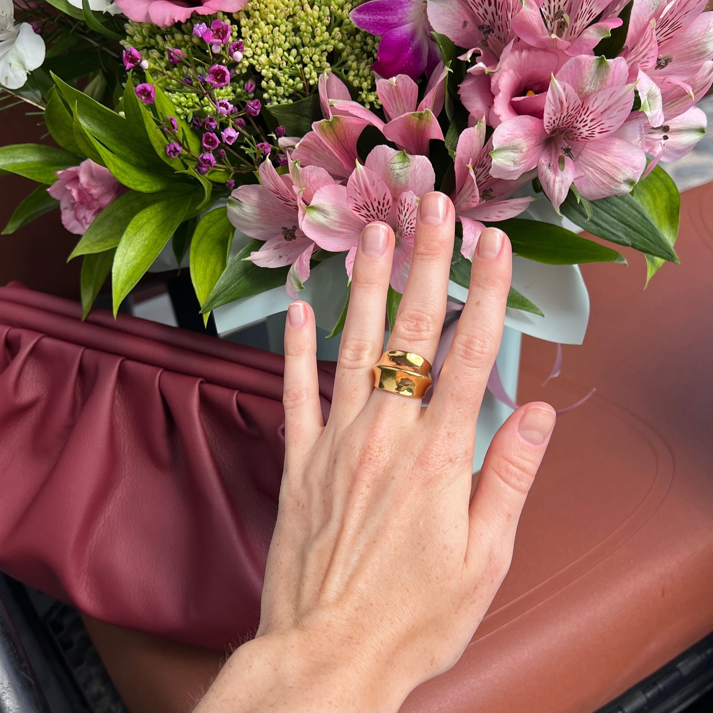 Hand wearing the fashionable dome ring in PVD-coated 18k gold-plated stainless steel resting beside a pink floral bouquet