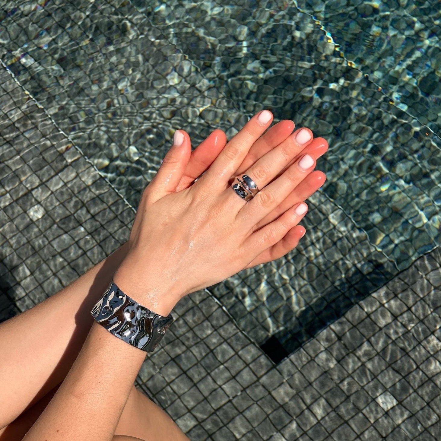 Hands wearing the fashionable dome ring in PVD-coated 925 silver-plated stainless steel with silver cuffs, resting at the edge of a pool to show its waterproof finish