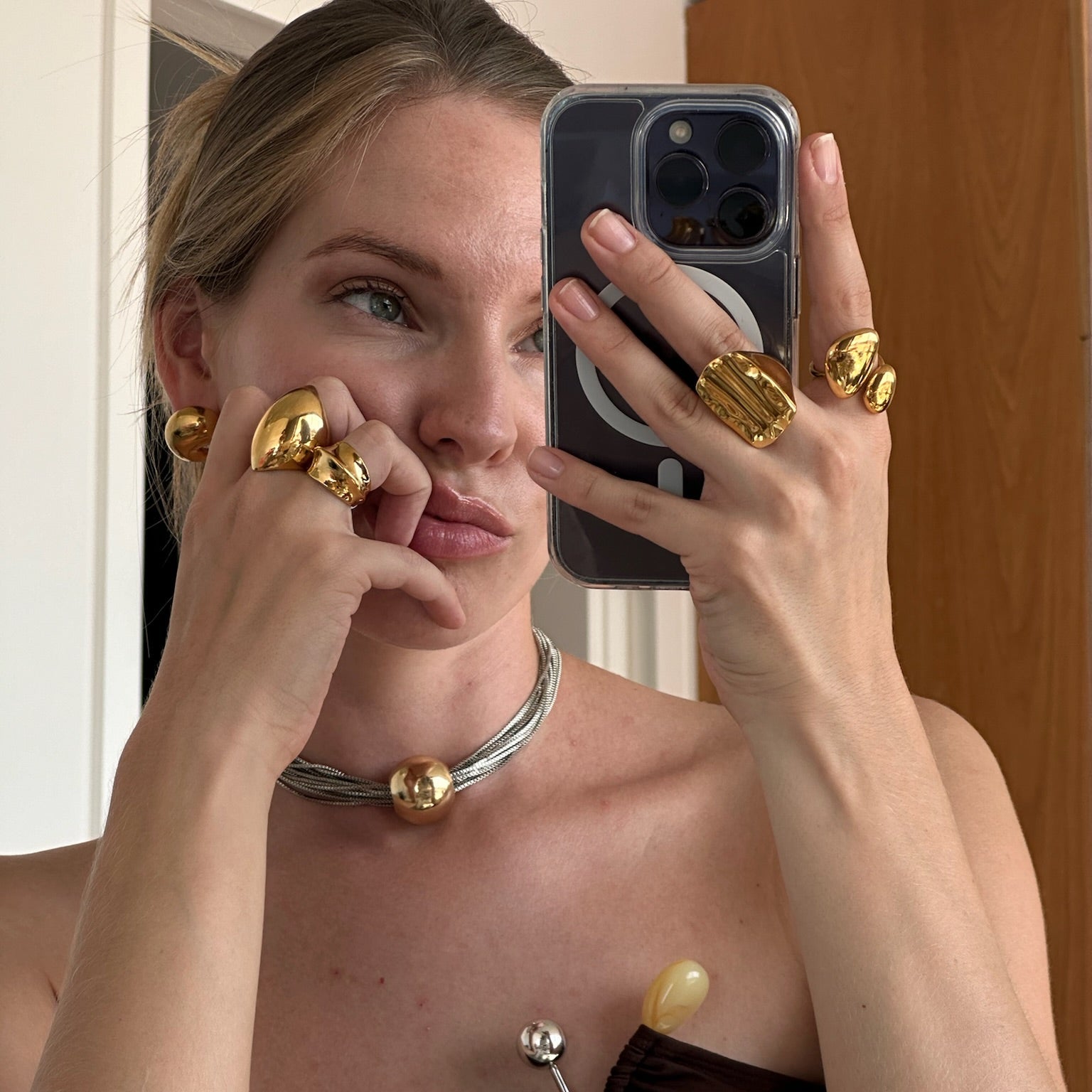 Model taking a mirror selfie wearing the fashionable dome ring in PVD-coated 18k gold-plated stainless steel stacked with gold rings and a gold necklace