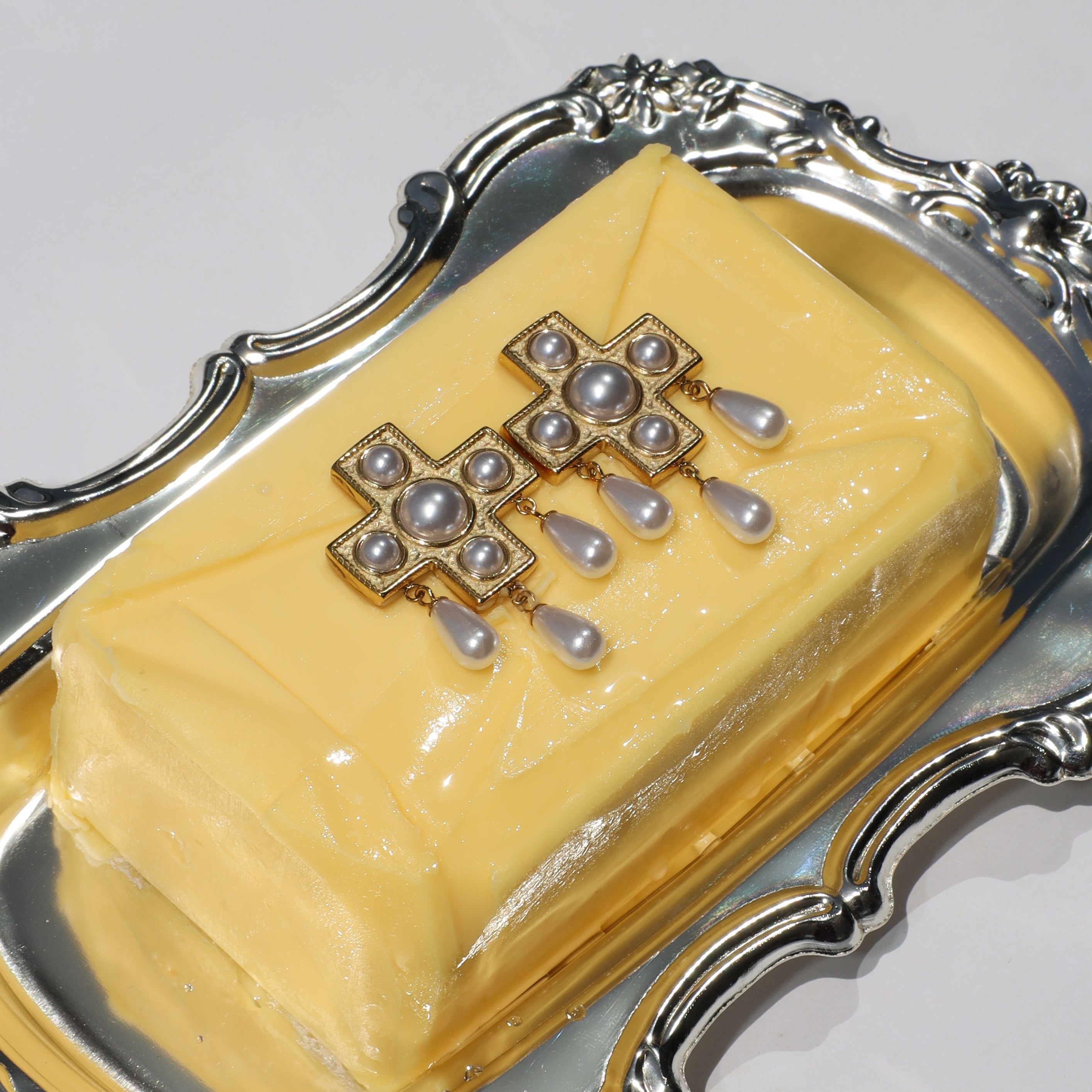 Pearls Before Drama gold cross drop earrings with cubic zirconia and faux-pearl drops, displayed on a silver tray