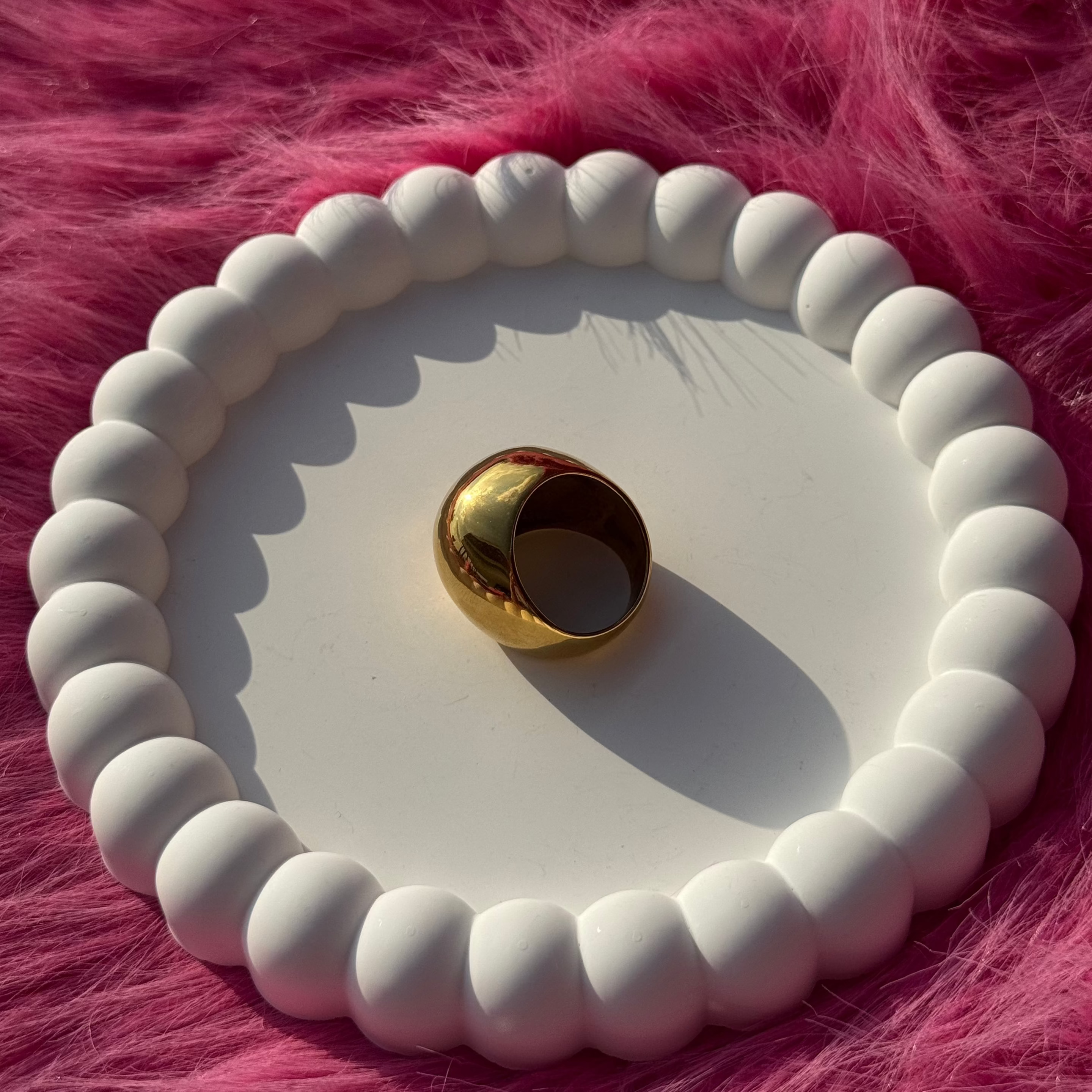 Side view of the ball ring in PVD-coated 18k gold-plated stainless steel on a white beaded dish against a pink fur background