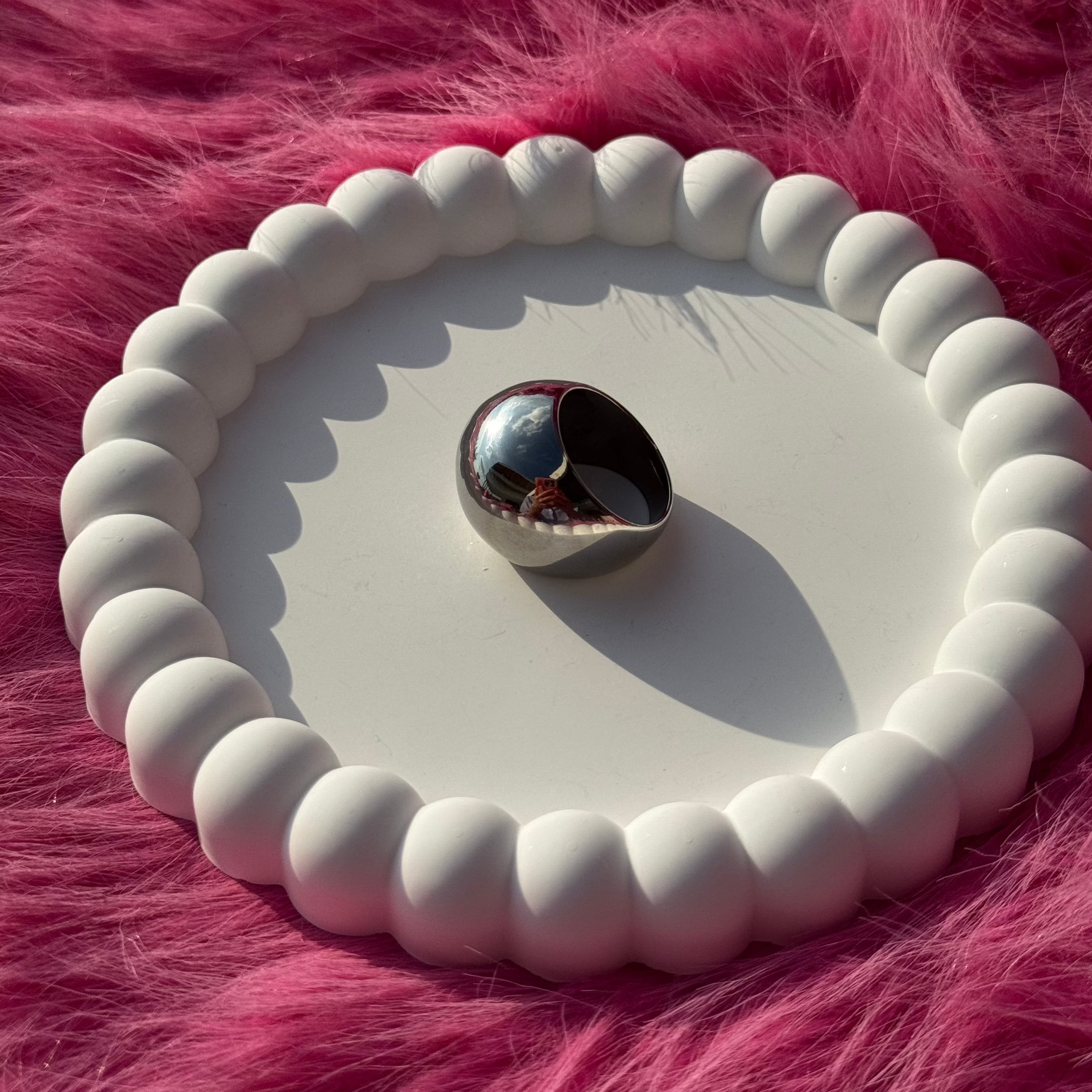 Single ball ring in PVD-coated 925 silver-plated stainless steel displayed on a white beaded dish against a pink fur background