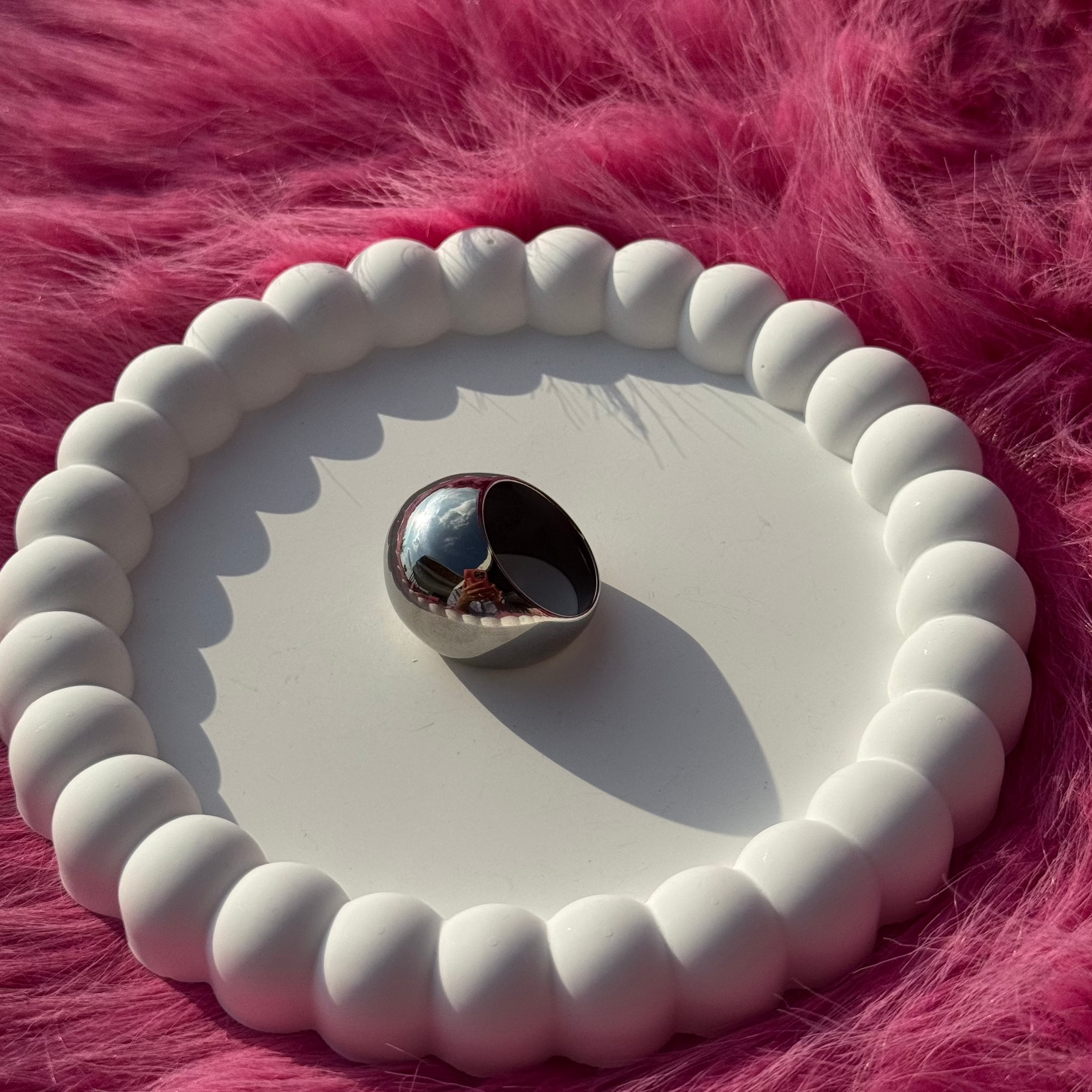 Side view of the ball ring in PVD-coated 925 silver-plated stainless steel on a white beaded dish against a pink fur background