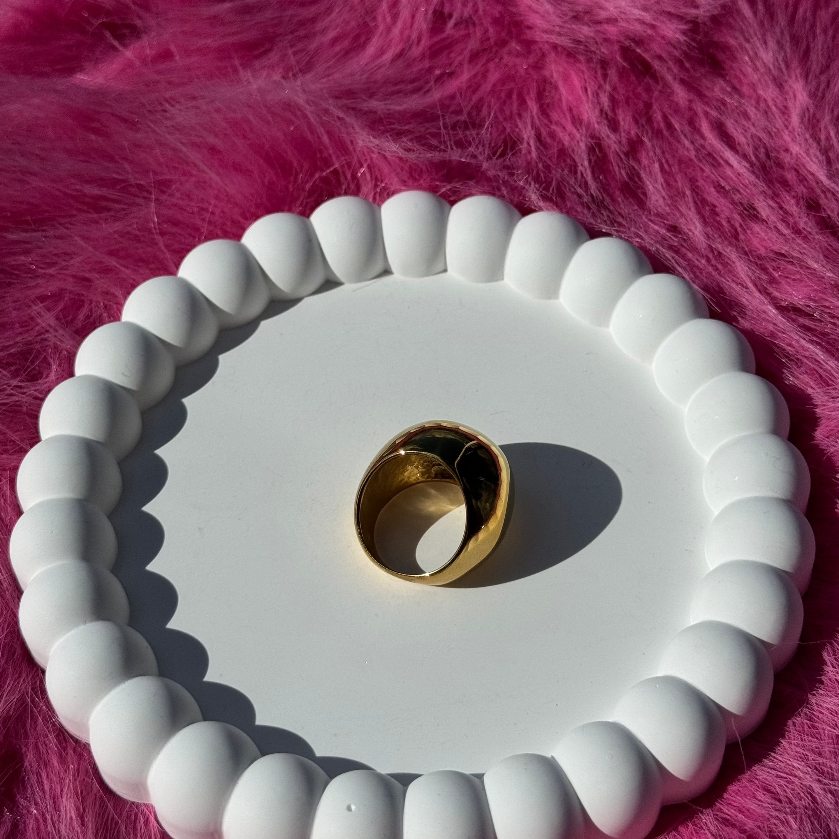 Top view of the ball ring in PVD-coated 18k gold-plated stainless steel on a white beaded dish against a pink fur background