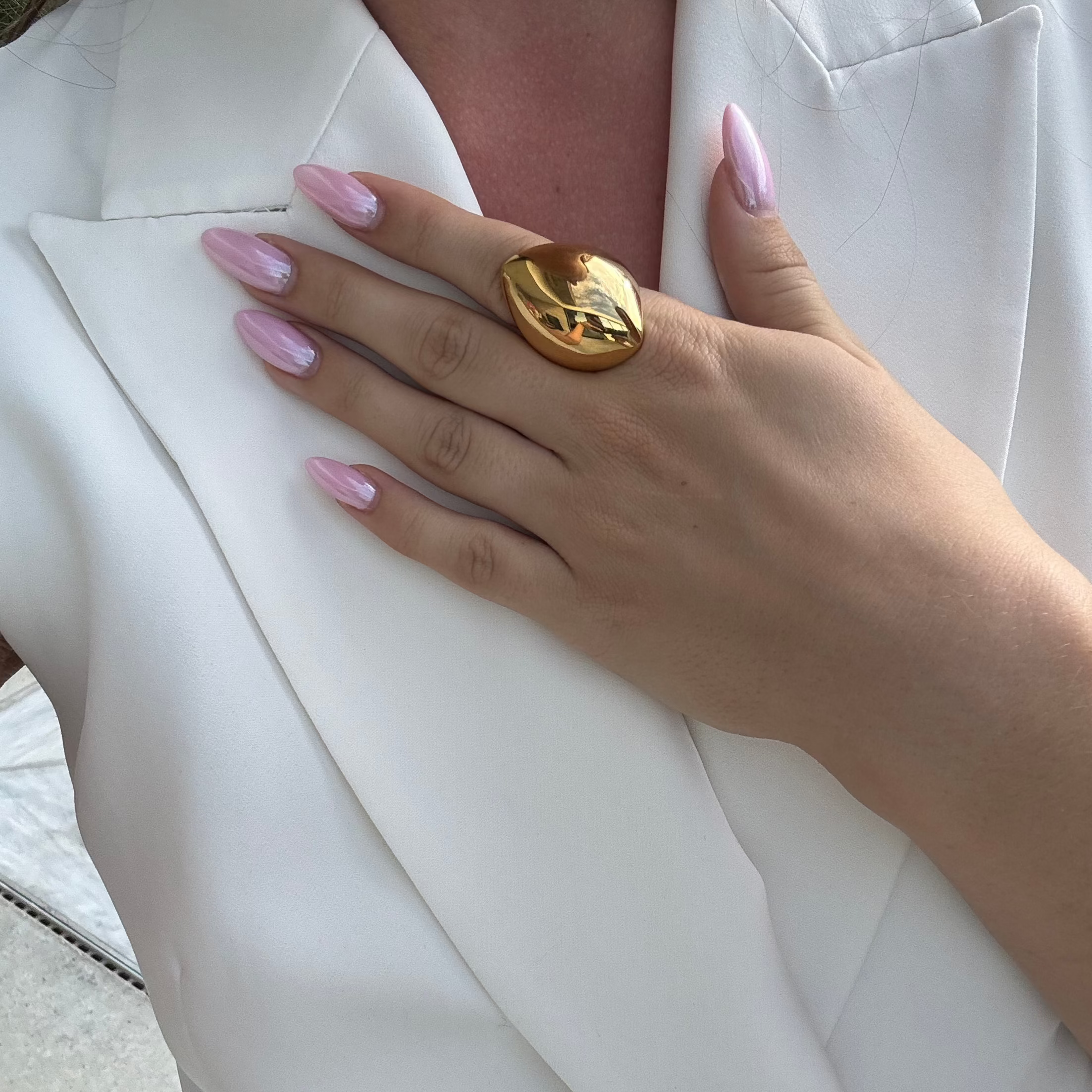 Model wearing the angular statement ring in PVD-coated 18k gold-plated stainless steel on her finger against a white blazer